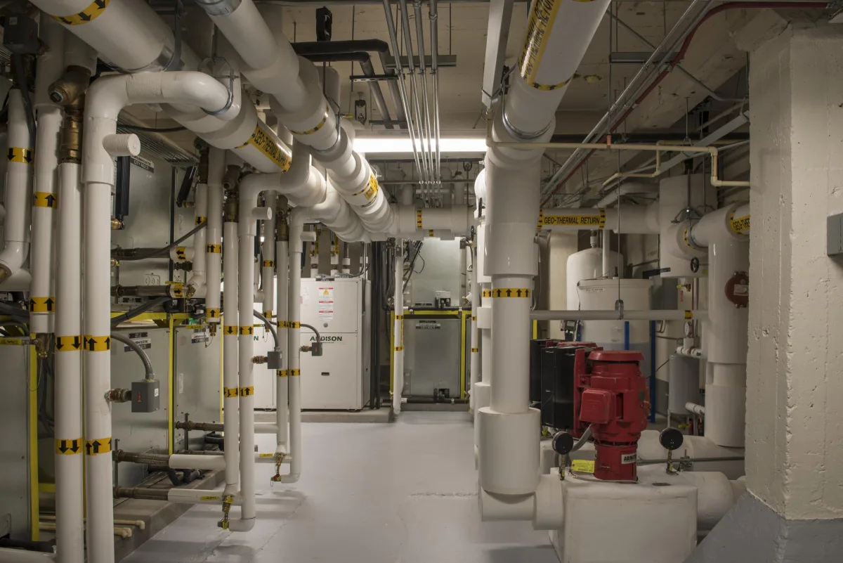 A clean basement mechanical room with labeled white pipes, valves and pumps