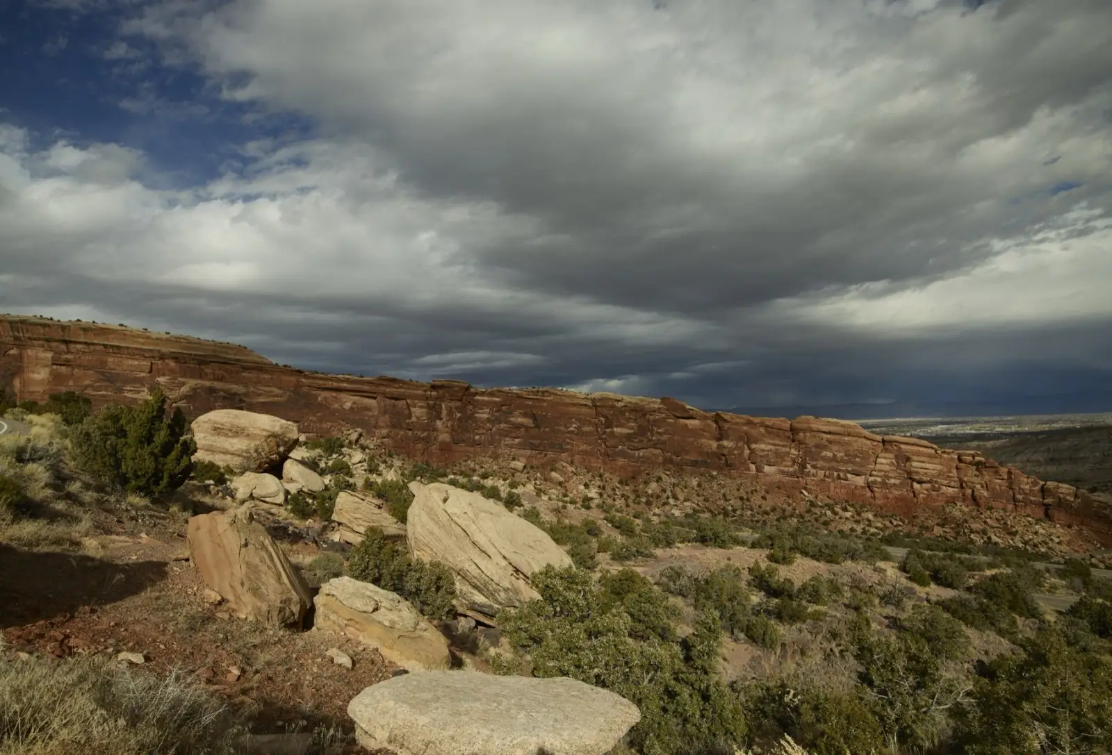 Layered canyon rim, boulders and high-desert vegetation under a dramatic cloud-filled sky