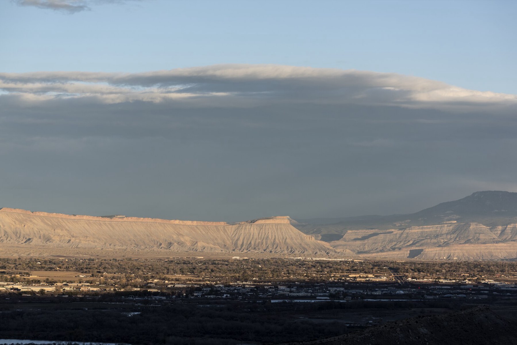 A wide Grand Valley view with sunlit Book Cliffs and blue-gray clouds