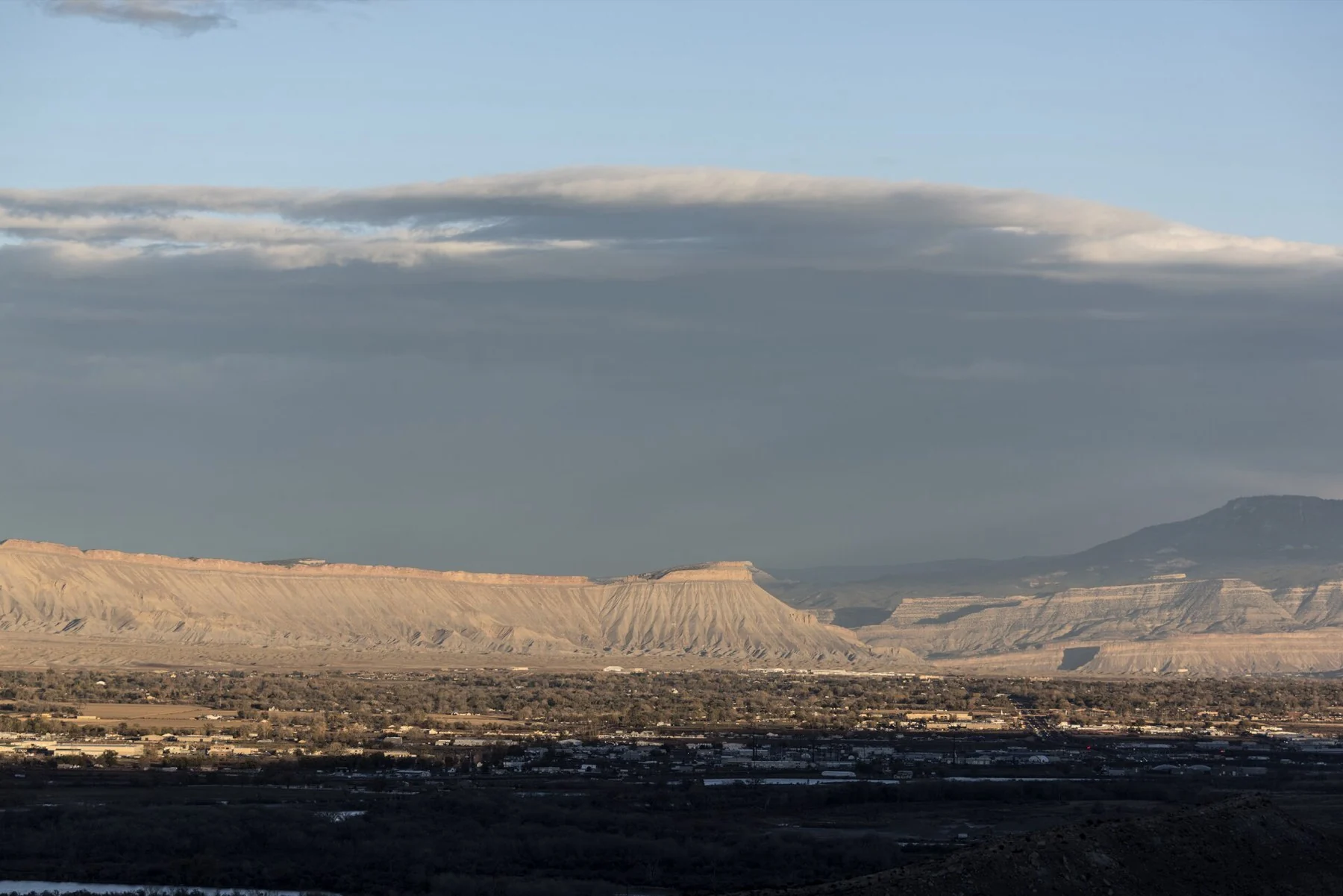 A wide Grand Valley view with sunlit Book Cliffs and blue-gray clouds