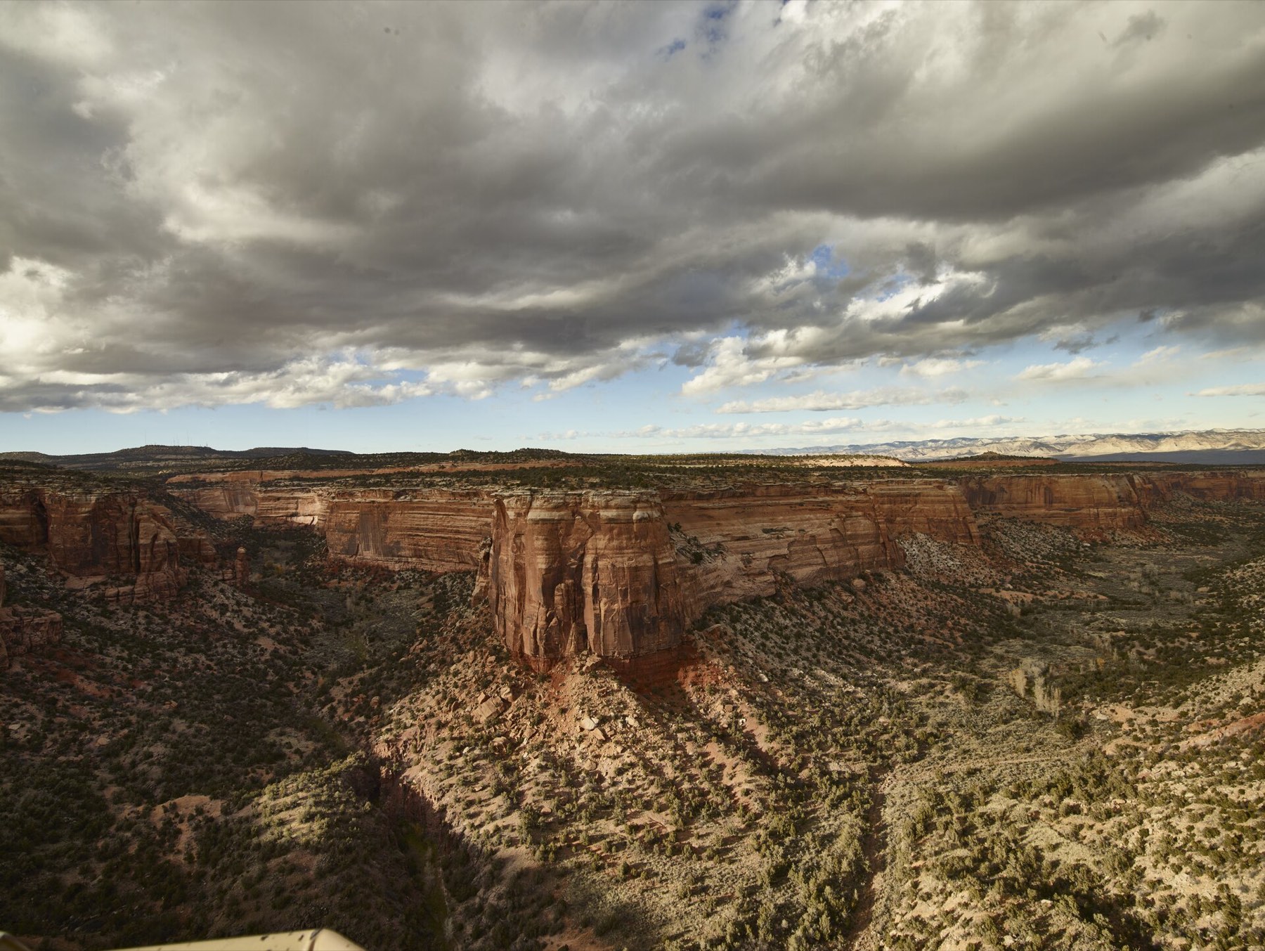 A broad sandstone canyon overlook with towering rock walls and broken cloud shadows